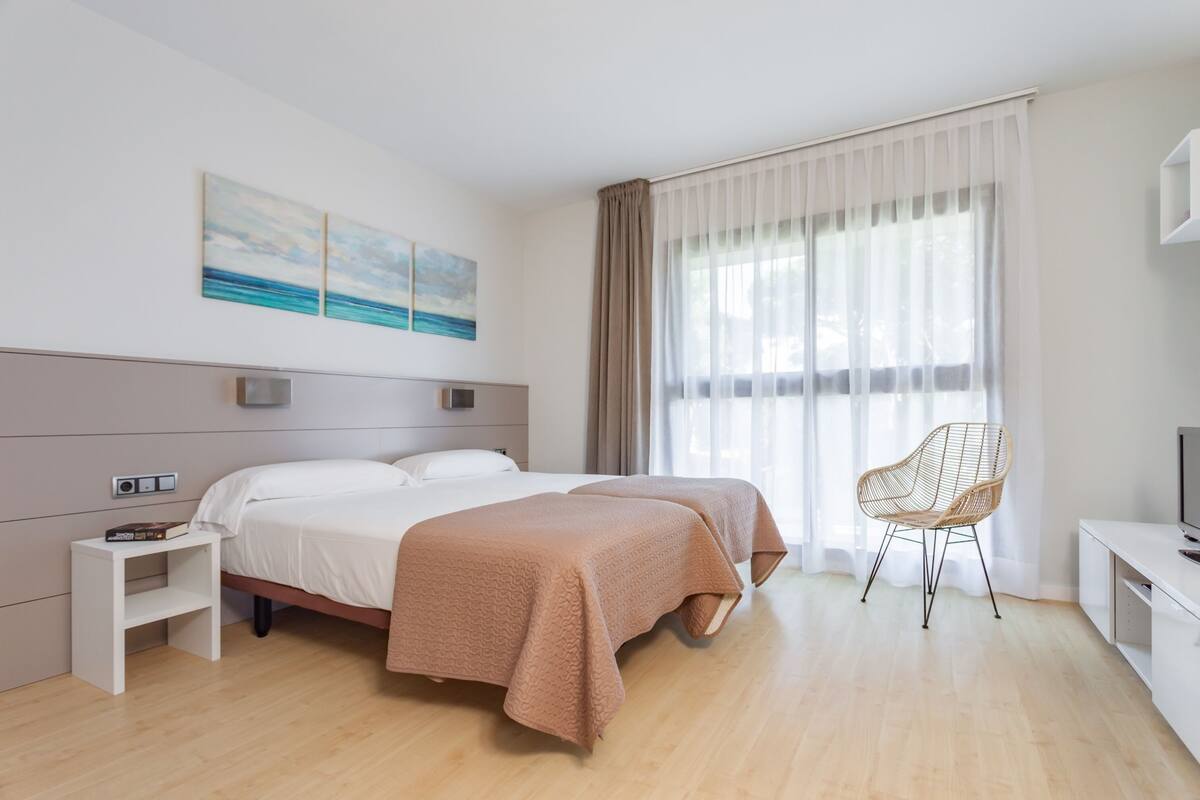 Une chambre d’hôtel moderne équipée de deux lits, d’une télévision, d’une chaise et d’œuvres d’art accrochées au mur.