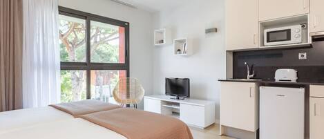 Habitación de hotel moderna con cama, televisor, kitchenette pequeña y vista al exterior.