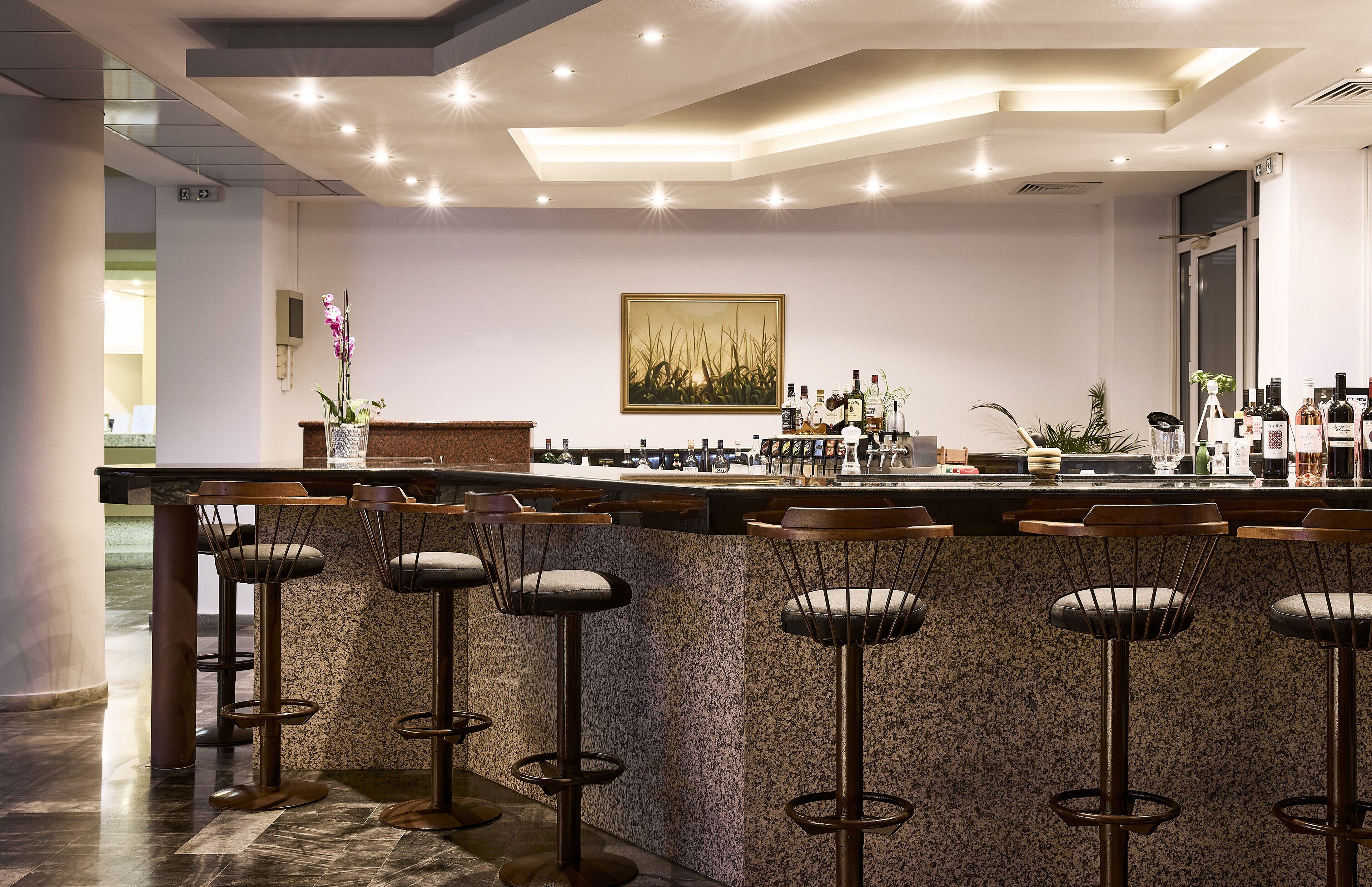 A modern bar area with a granite countertop, bar stools, and a variety of bottles.