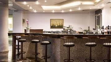 A modern bar area with a granite countertop, bar stools, and a variety of bottles.