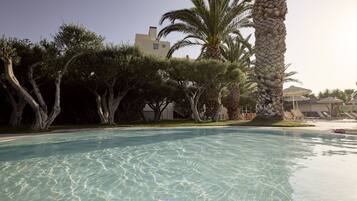 A clear swimming pool surrounded by trees and a building in the background.