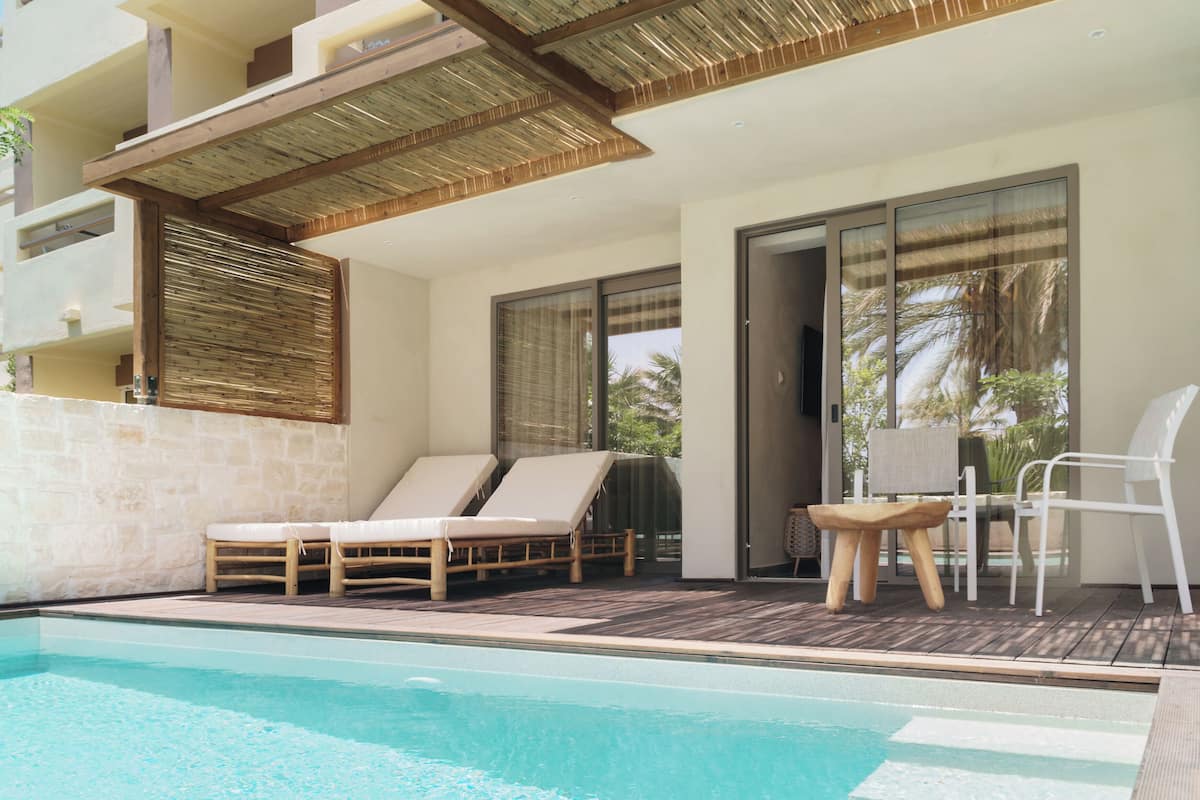 A pool area with lounge chairs and a table, a stone wall, and a wooden deck.