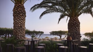 Un área de estar al aire libre con mesas y sillas, palmeras y vista al mar.