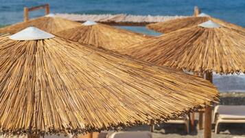 A beach with straw umbrellas and lounge chairs.