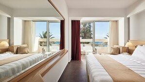 Habitación de hotel con dos camas, un espejo grande y vista al océano.