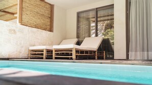 Un área de piscina moderna con sillones de descanso, un muro de piedra y un ventanal con vistas a la vegetación.