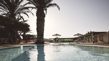 Una piscina al aire libre, sombrillas, sillones reclinables de piscina