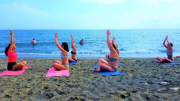 A beach with people practicing yoga on mats.