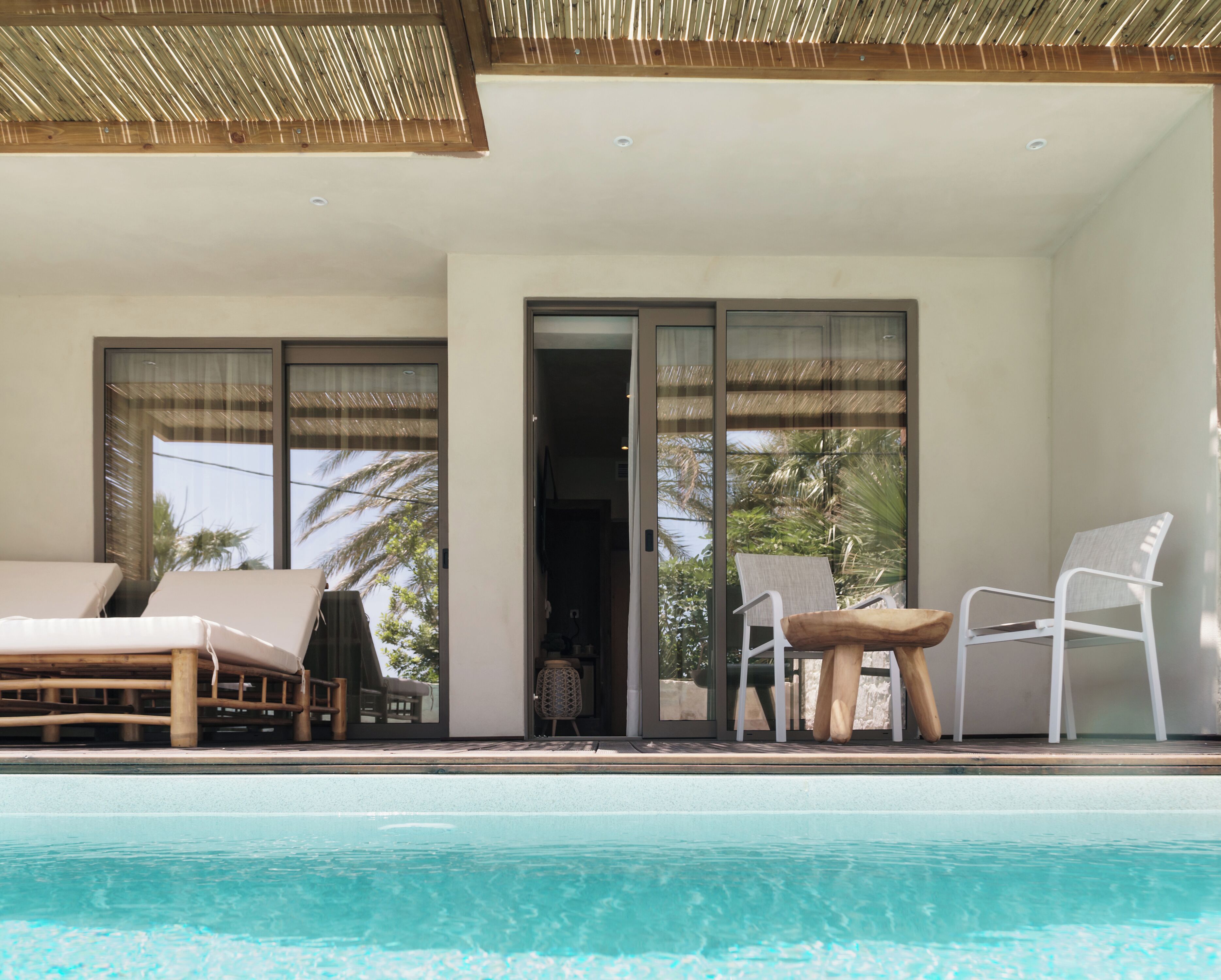 A poolside area with lounge chairs and a table, a covered seating area with a view of palm trees, and a sliding glass door leading to an interior space.