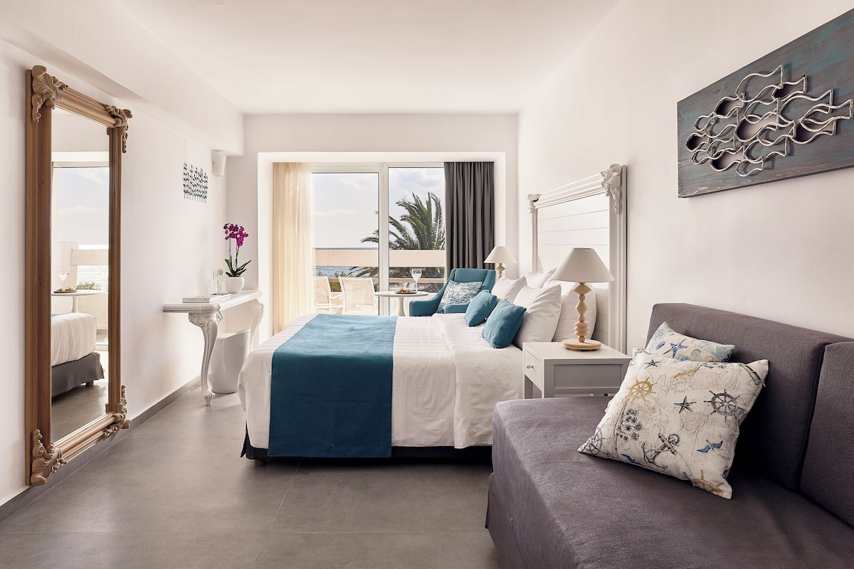 A hotel room with a large bed, a sofa, a desk, and a balcony with a view.