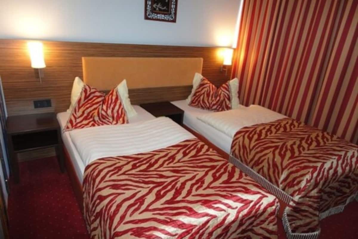 A hotel room with two beds, each with zebra-patterned bedding, wooden headboards, and bedside lamps.
