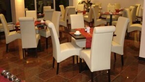 A restaurant with multiple tables and chairs, a red tablecloth on one table, and a tiled floor. - Grand Hotel Dream Frankfurt City (Frankfurt)