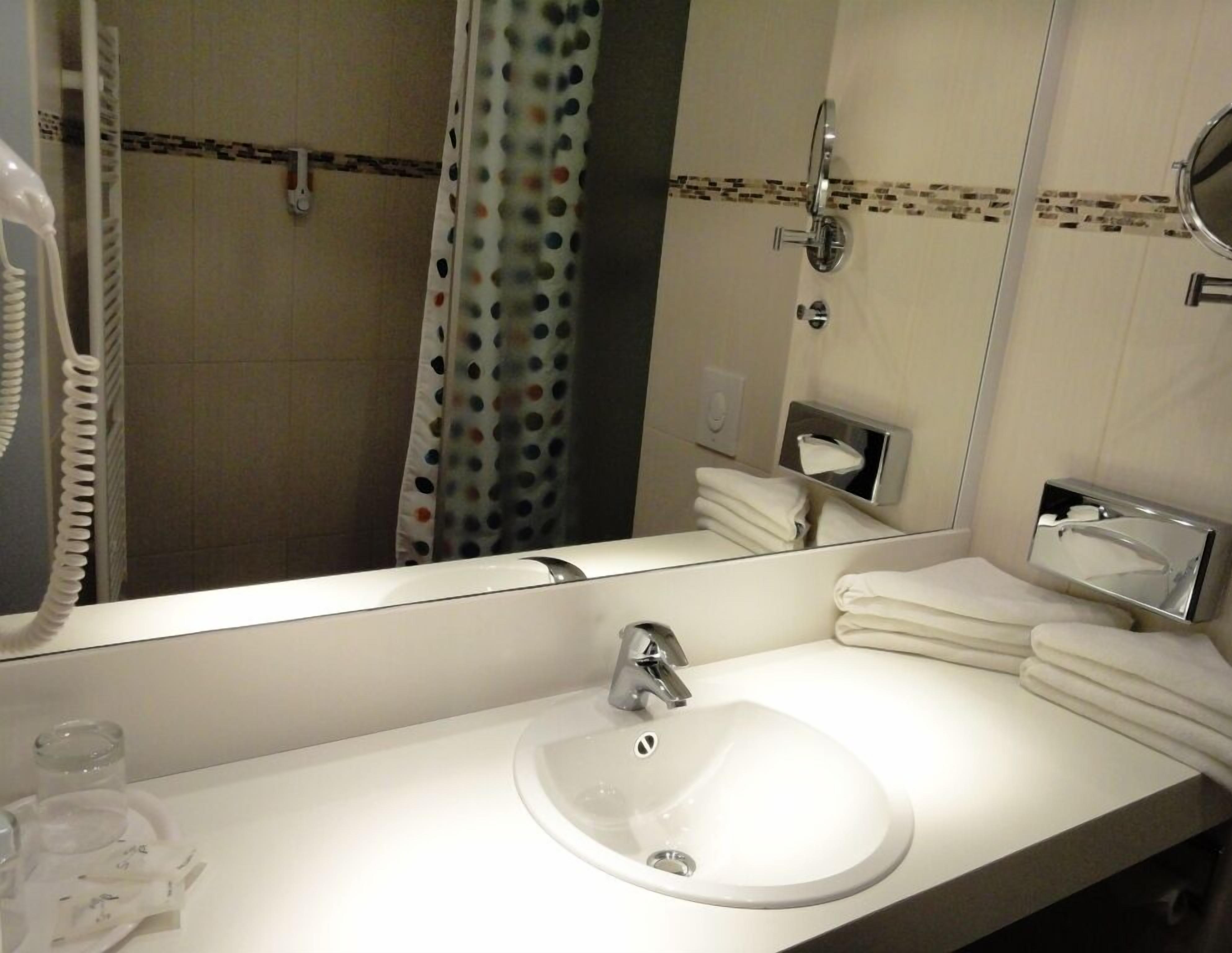 Ein Badezimmer mit einem weißen Waschbecken, einem Spiegel, einem Handtuchhalter und einer Duschvorhang.
