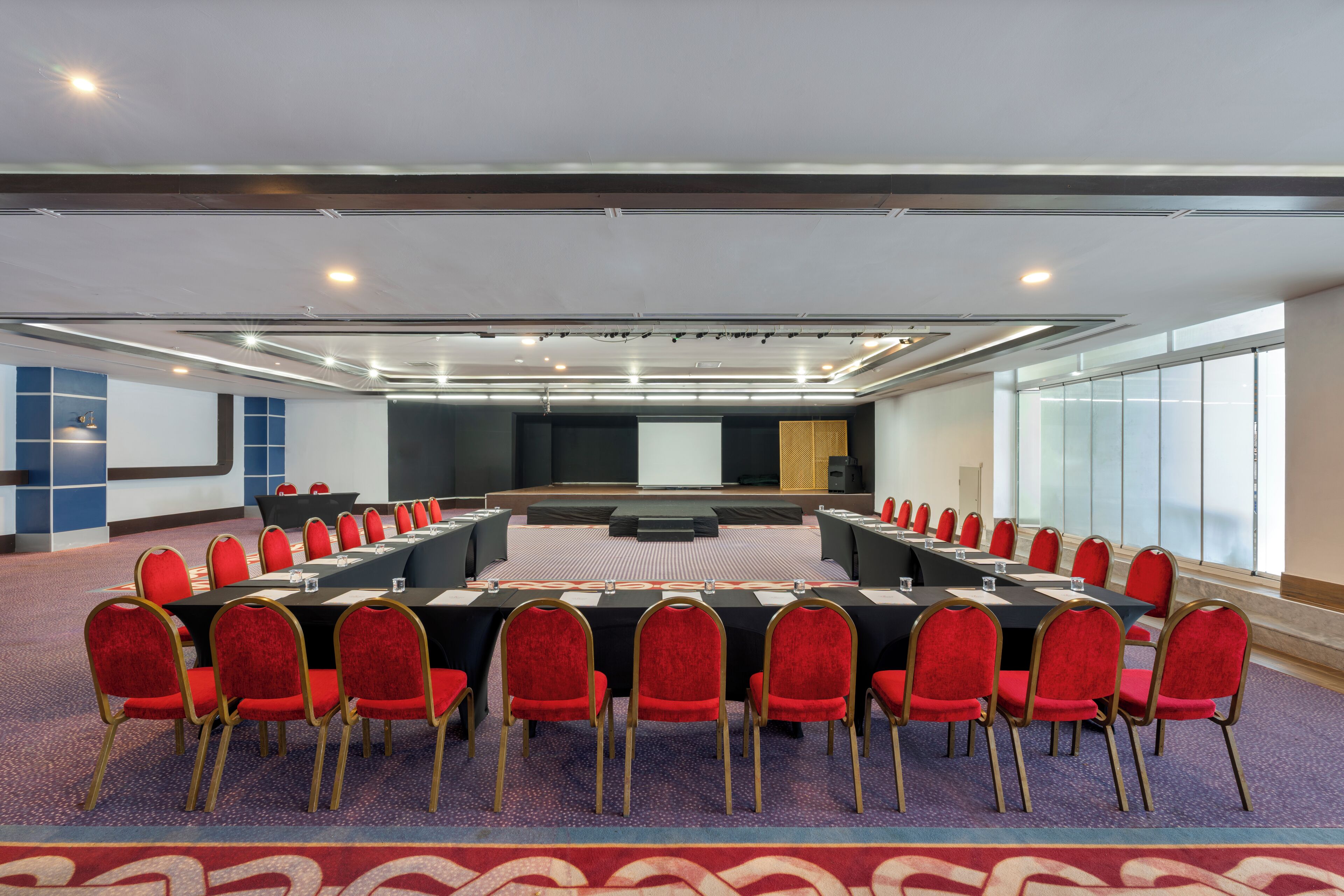 A conference room with a long table, red chairs, and a carpeted floor.