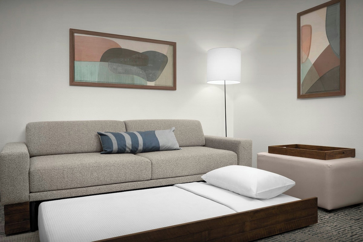 Ett modernt hotellrum med en soffa, en säng, ett sängbord och två abstrakta tavlor på väggen.