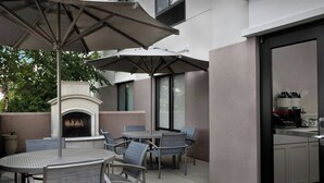 Un patio al aire libre con una mesa redonda y sillas, un paraguas grande y una chimenea.
