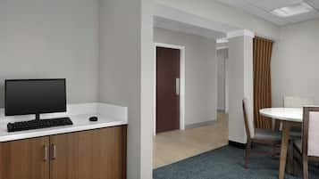 A modern office space with a computer setup, a meeting table, and a door leading to another room.