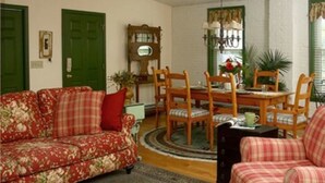 A living room with a floral sofa, a plaid armchair, a wooden dining table with chairs, a mirror, and a green door. - The Brafferton Inn (Gettysburg)