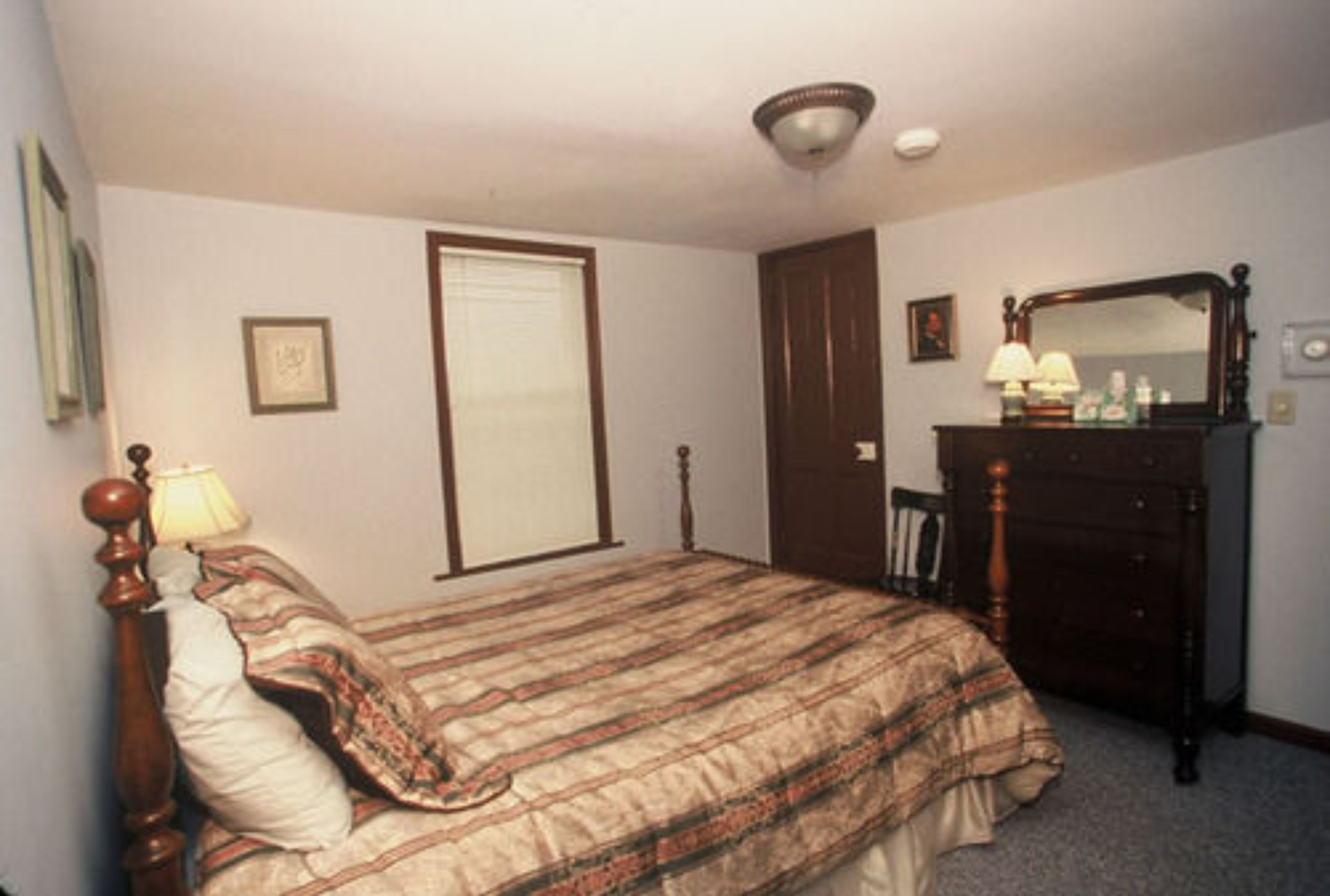 A bedroom with a bed, a dresser, a mirror, a lamp, and a door.