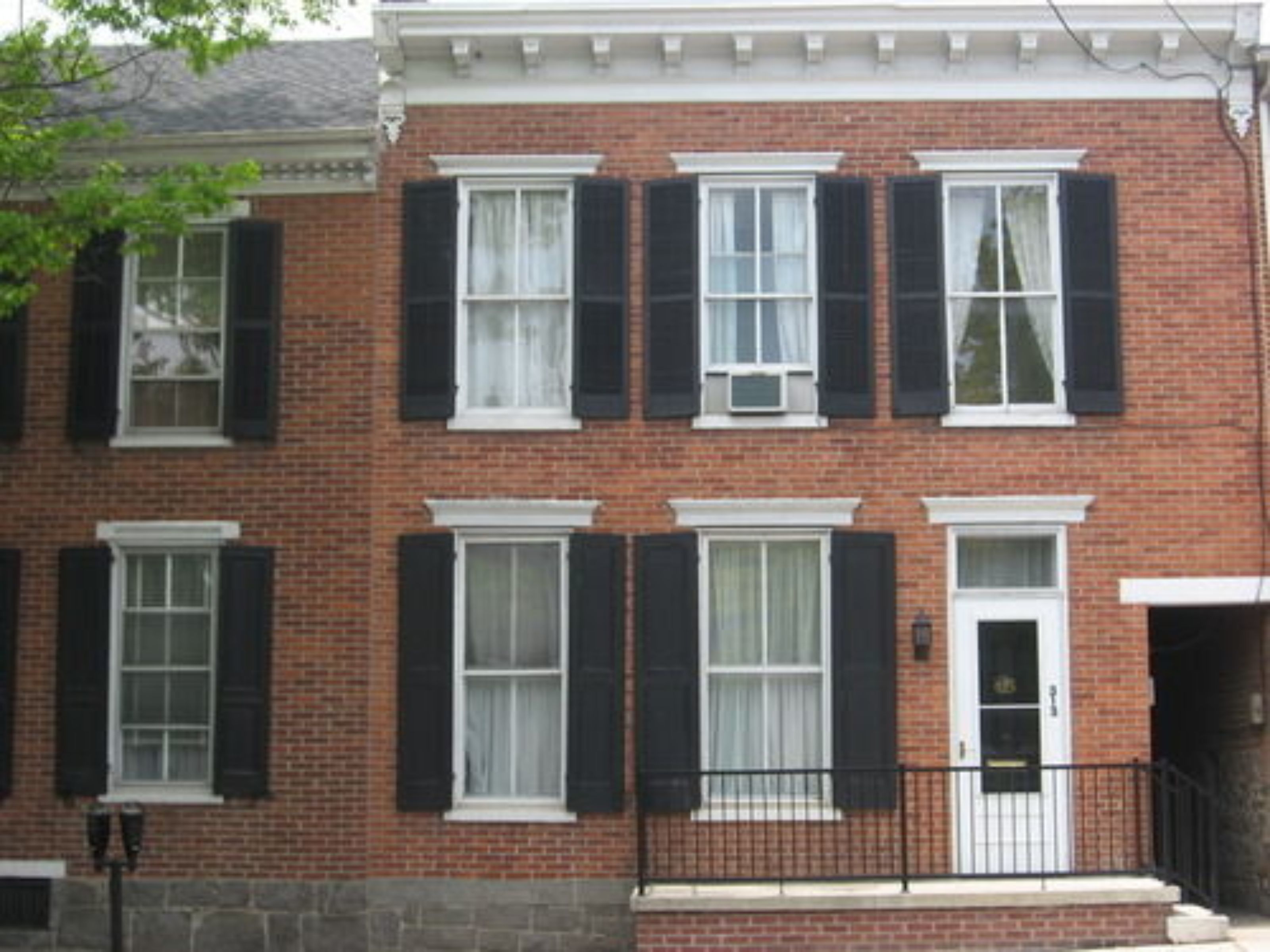 A two-story brick building with black shutters on the windows and a white door.