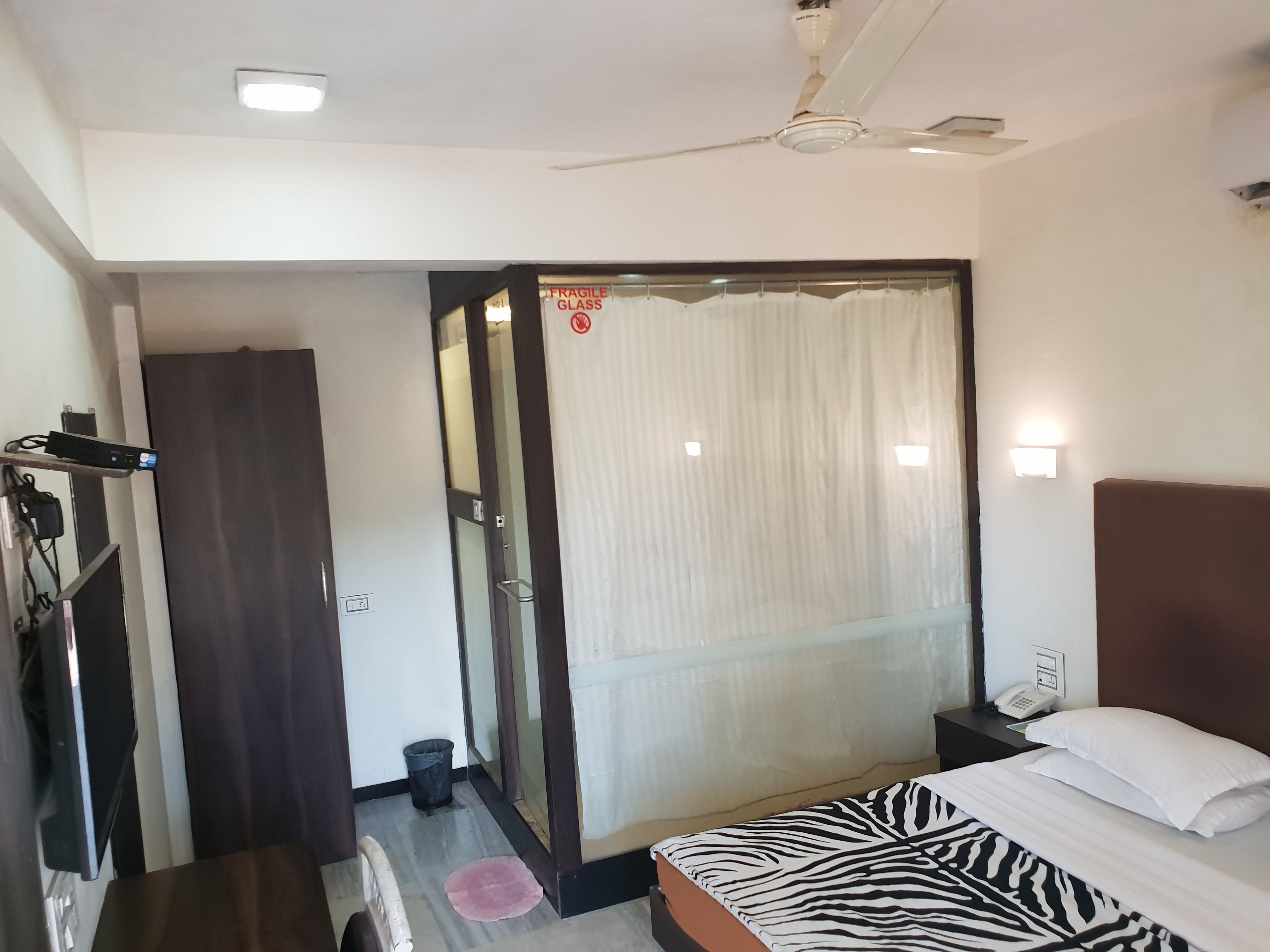 Una habitación de hotel con una cama, un escritorio con una computadora, un teléfono y un ventilador de techo.