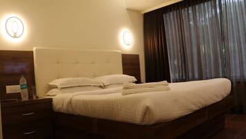 Una habitación de hotel con una cama grande, dos mesitas de noche, una botella de agua y una mesilla.