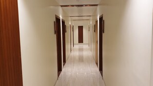 A long, narrow hallway with wooden doors on both sides and a marble floor. - Hotel Milan International (Mumbai)