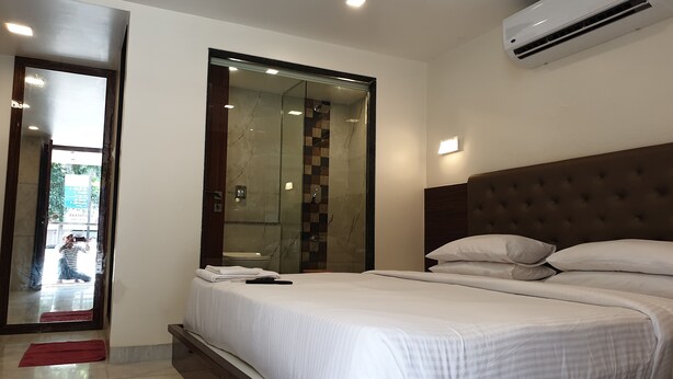 A hotel room with a large bed, a built-in wardrobe, a shower area, and an air conditioning unit. - Hotel Milan International (Mumbai)