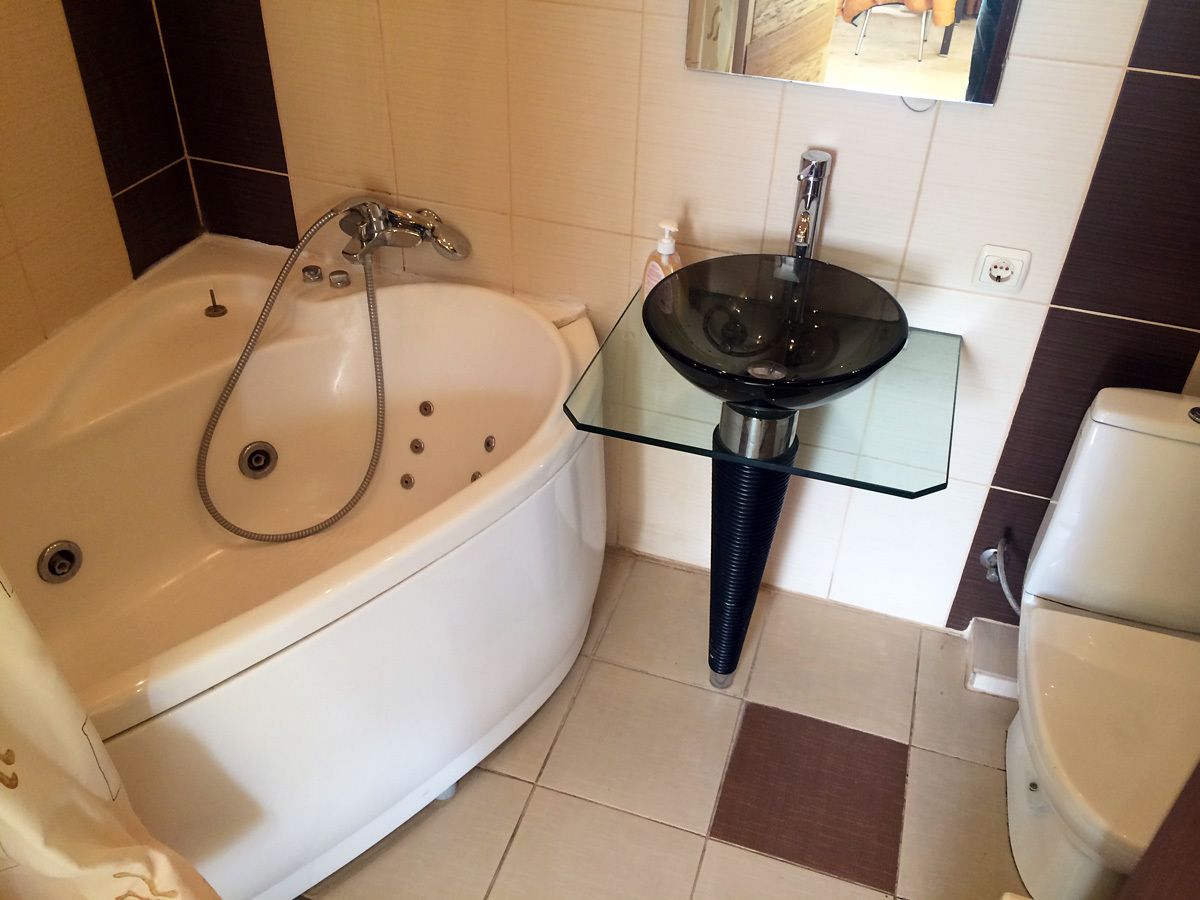 A bathroom with a bathtub, a glass sink, and a toilet.