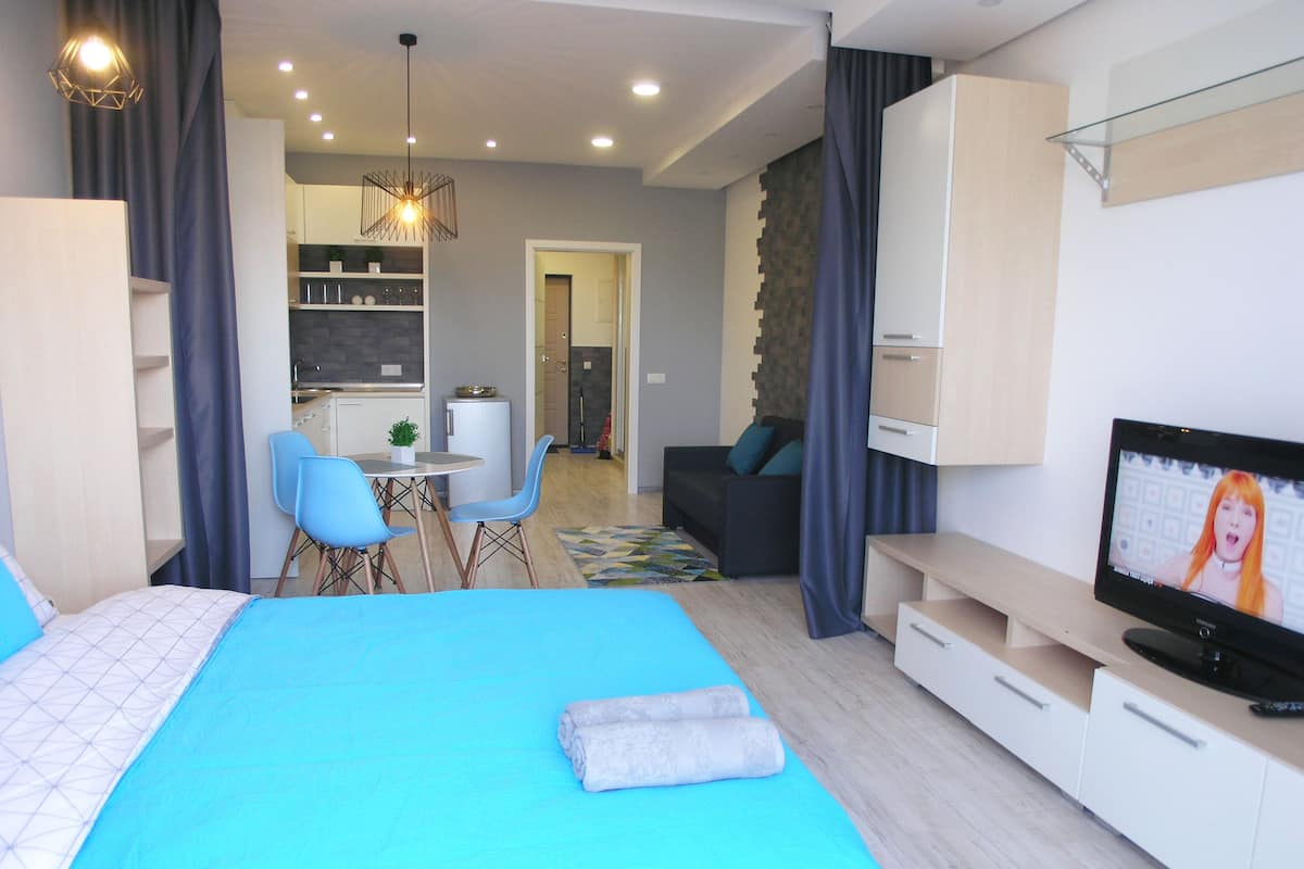 A modern hotel room with a large bed, a TV, a desk, and a dining area.