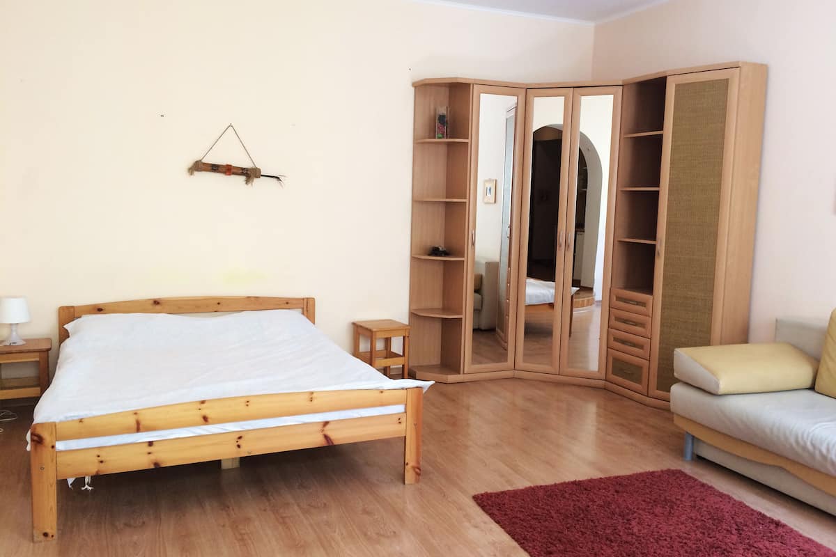 A bedroom with a wooden bed, a wardrobe, a small bedside table, and a red rug.