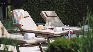 Zona junto a la piscina con sillones de descanso, toallas y una botella de protector solar.