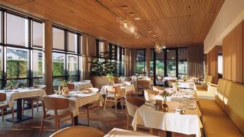 Un restaurant doté de nombreuses tables et chaises, de grandes fenêtres et d’un plafond en bois.
