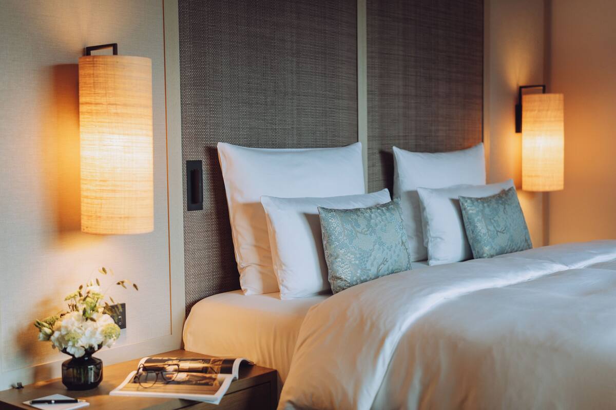 Une chambre d’hôtel avec un lit soigneusement fait, une table de chevet avec une lampe et un vase rempli de fleurs.