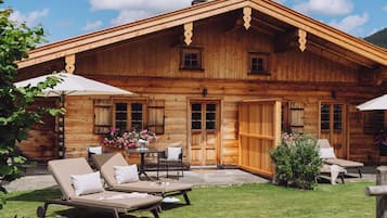 A wooden cabin with a patio, lounge chairs, and a table with flowers.