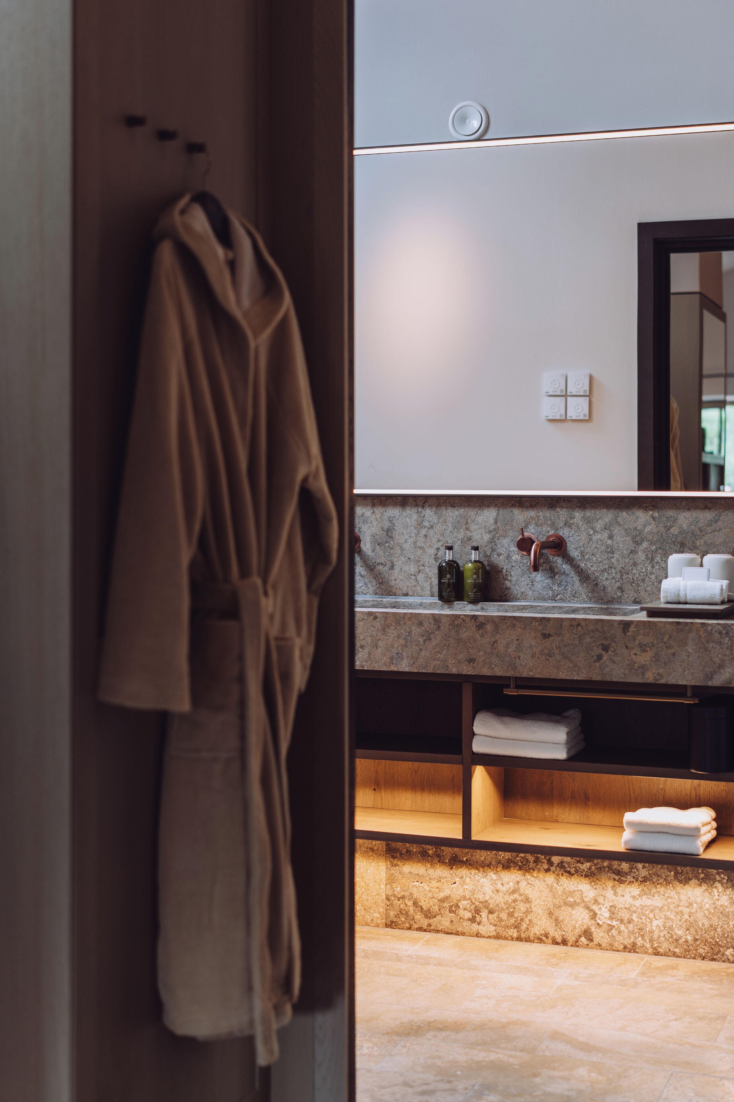 A bathroom with a robe hanging on a rack, a sink with toiletries, and a mirror.