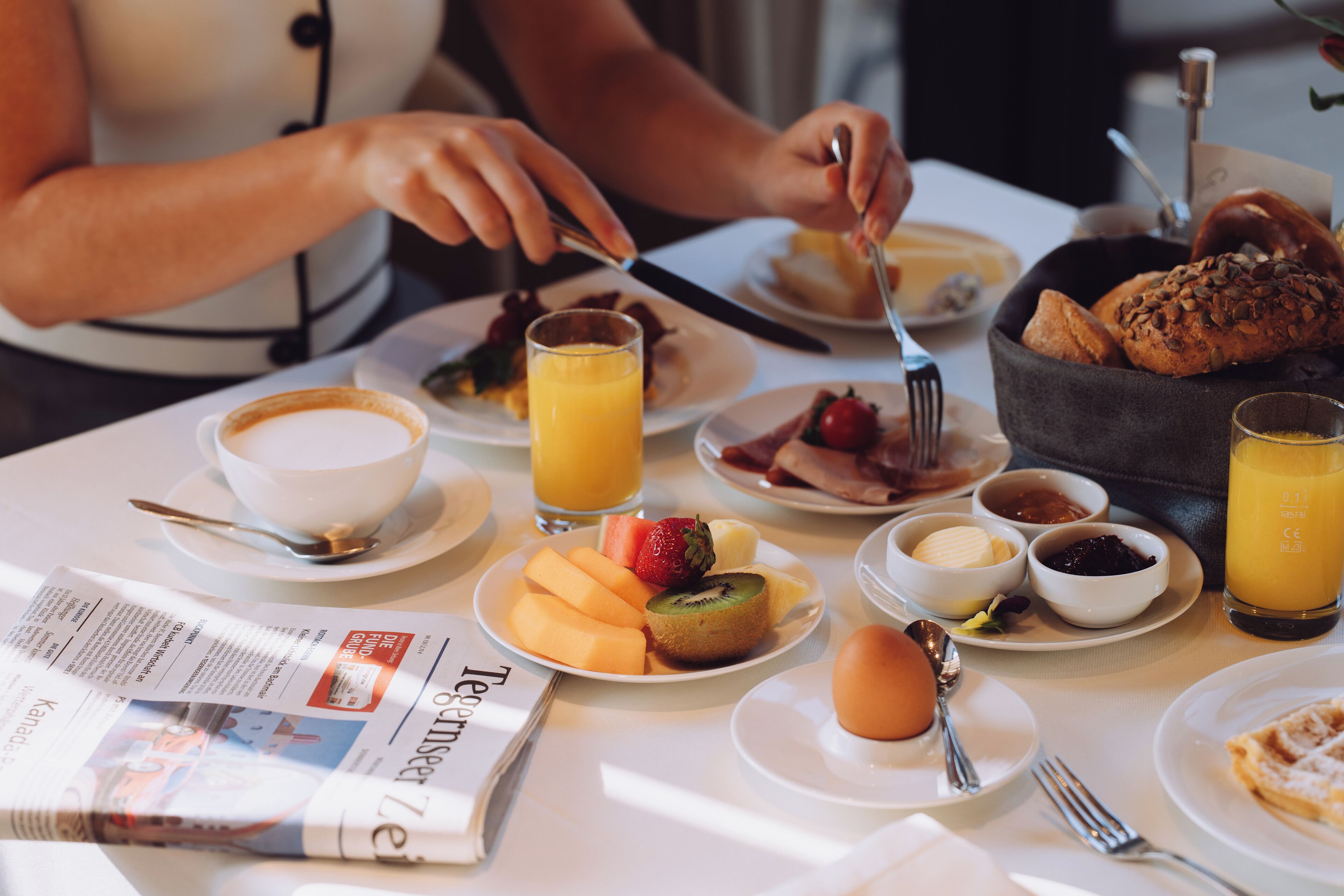 Un desayuno con diversos alimentos, utensilios y un periódico sobre una mesa.
