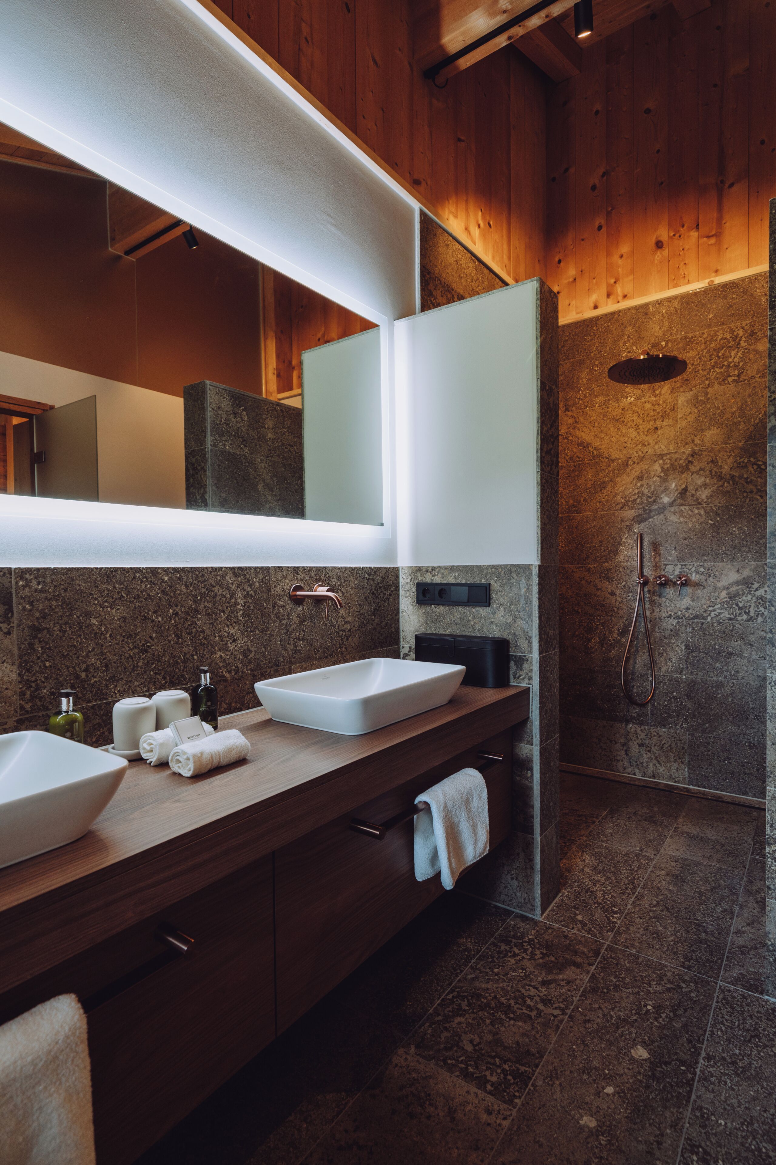 A modern bathroom with a wooden vanity, two sinks, a large mirror, and a shower area.