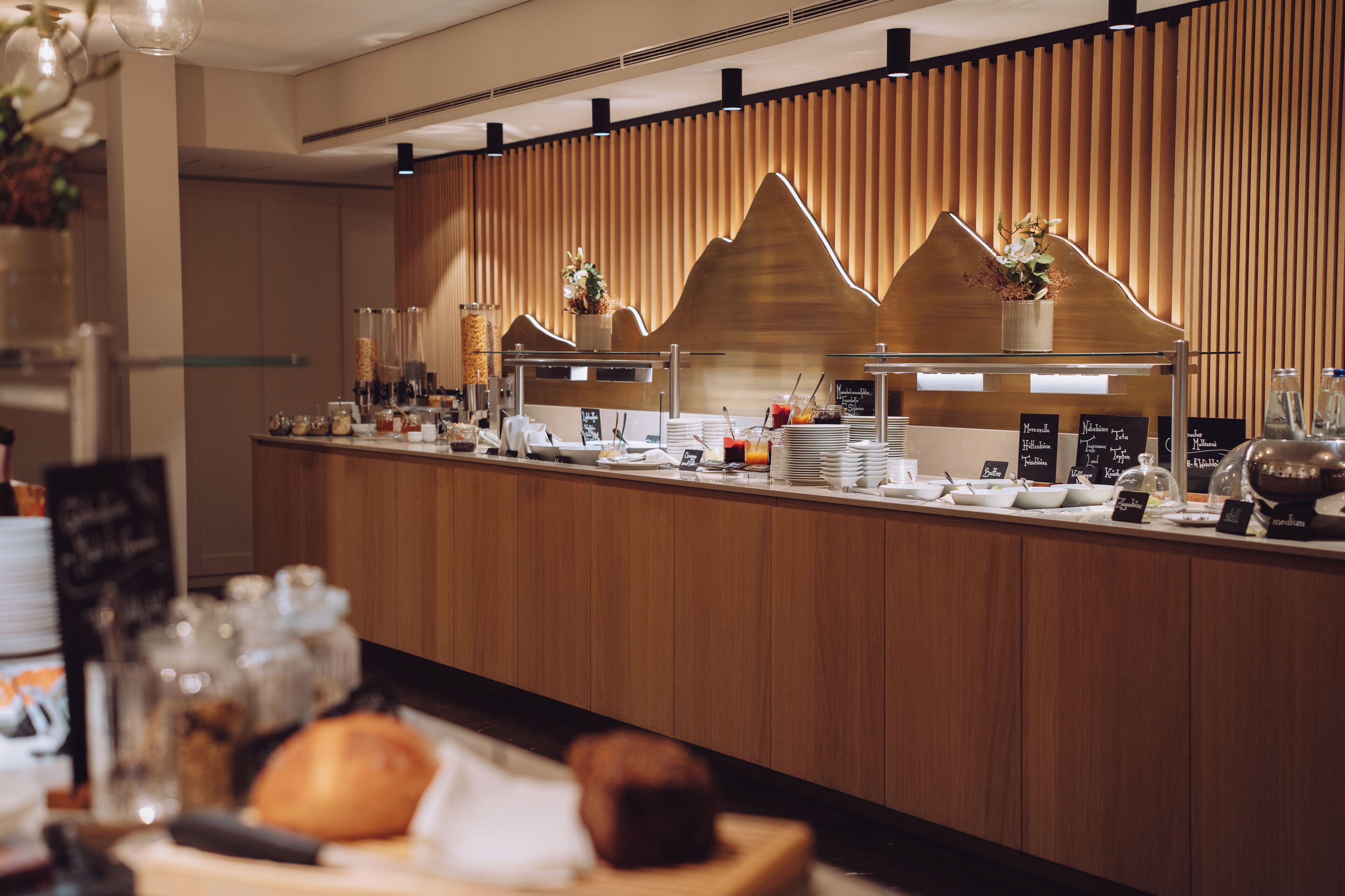 A breakfast bar with a wooden backdrop, various food items, and a coffee station.