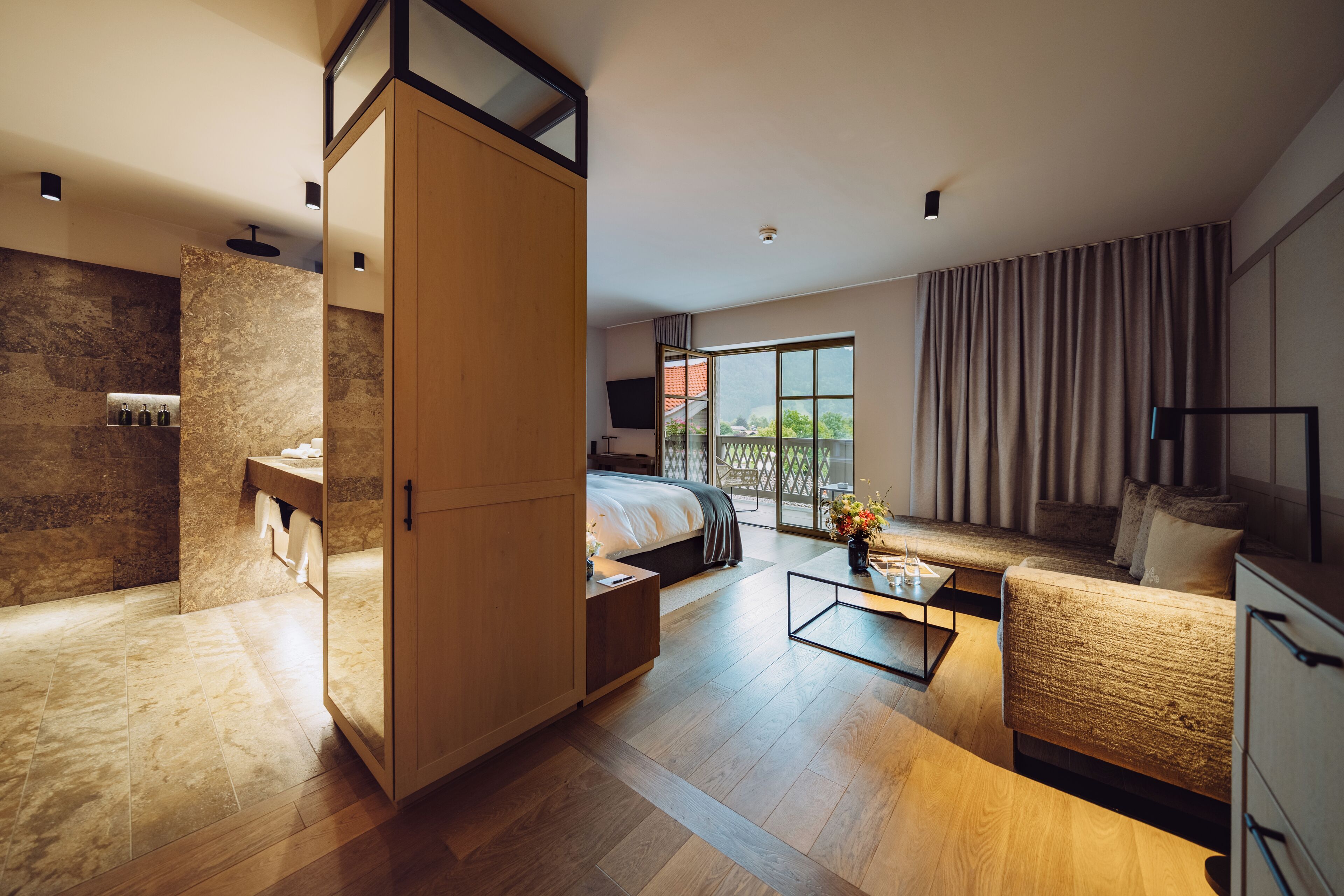 Moderni hotellihuone, jossa on sänky, sohva, sohvapöytä, suihkulla varustettu kylpyhuone ja parveke, jolta on näkymä.