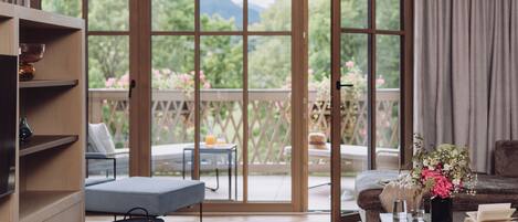 Ein Zimmer mit einer Schiebetür zum Balkon, einem Sofa, einem kleinen Tisch mit Blumenvase und einem Bücherregal.
