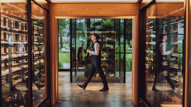 Un homme se promène dans un intérieur moderne, de part et d’autre se trouvent des vitrines, et au bout, une porte vitrée donne sur un jardin.