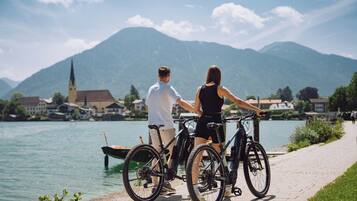 A couple standing by a lakeside path with bicycles, overlooking a town and mountains.