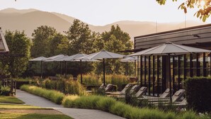 Une rangée de chaises longues avec des parasols, une allée pavée et, en arrière-plan, des arbres et des montagnes.