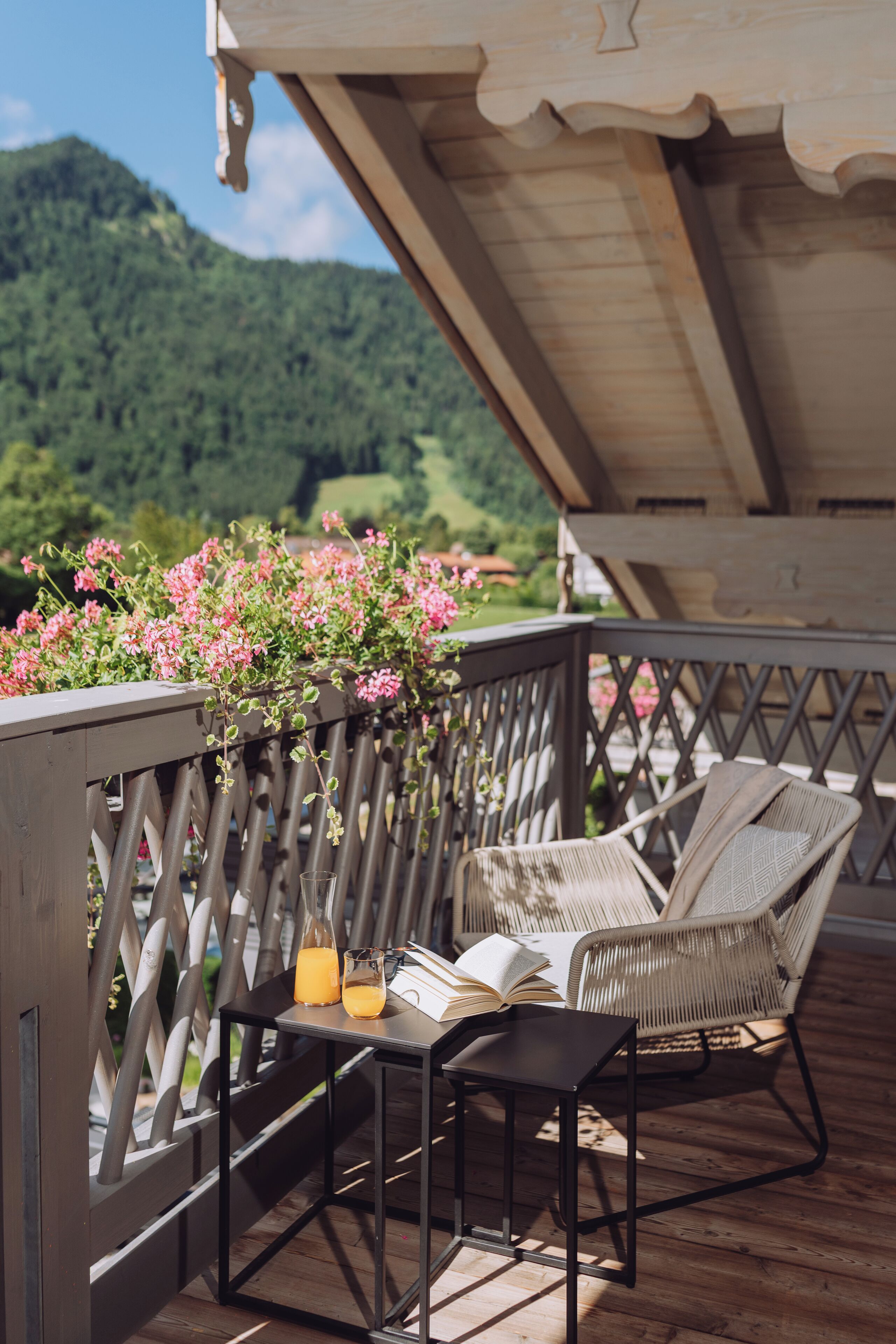 A wooden deck with a wicker chair and a small table, a glass of orange juice, and a book.