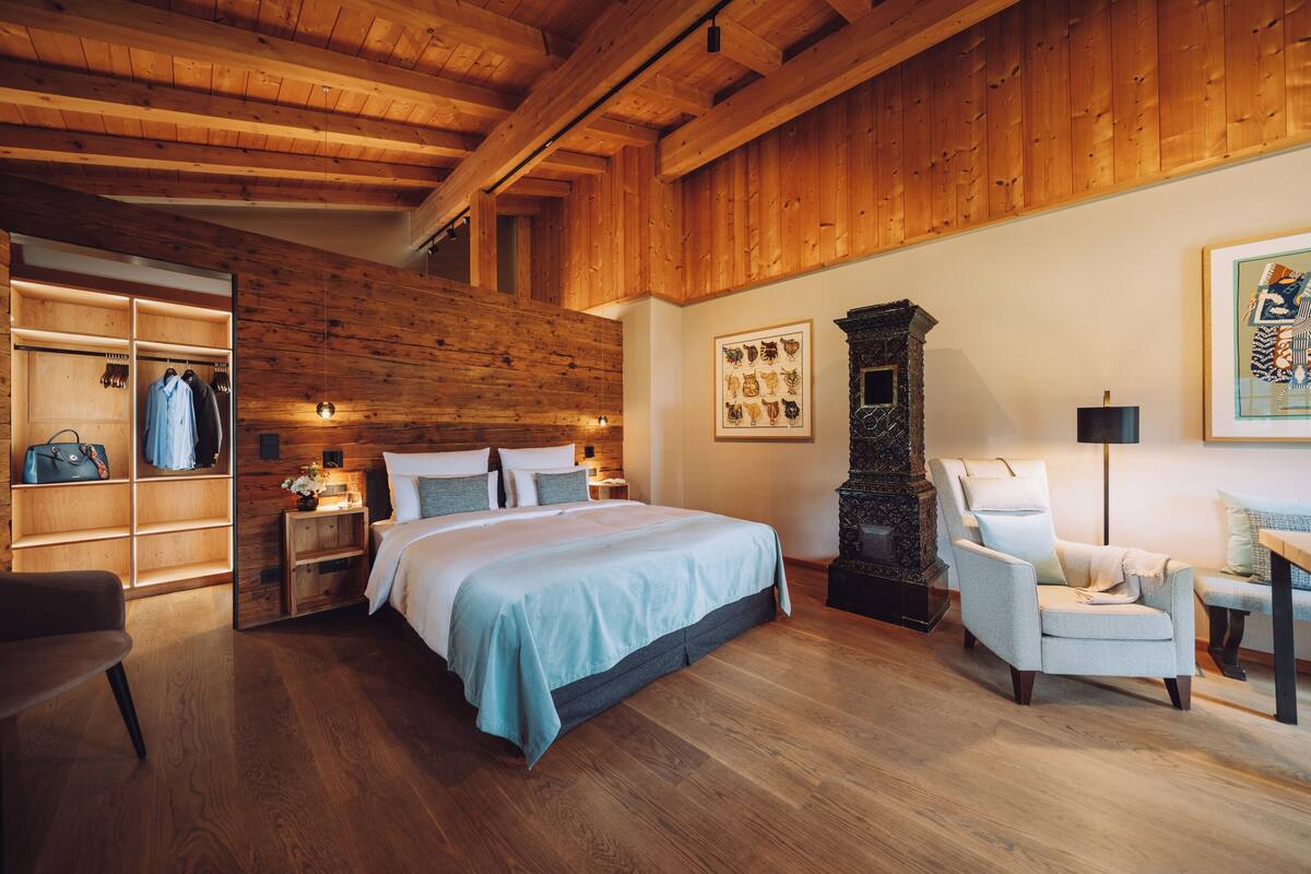 Une chambre avec un grand lit, un plafond en bois, une armoire, une cheminée et un fauteuil.