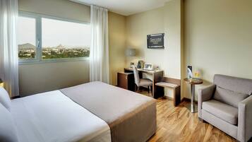 Ein Hotelzimmer mit Bett, Schreibtisch, Stuhl und Blick auf die Stadt.