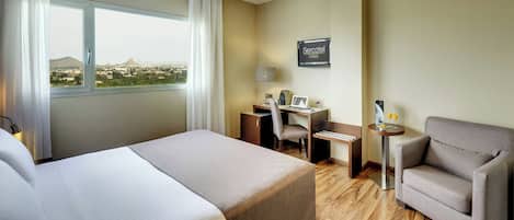 A hotel room with a bed, a desk, a chair, and a view of a cityscape.