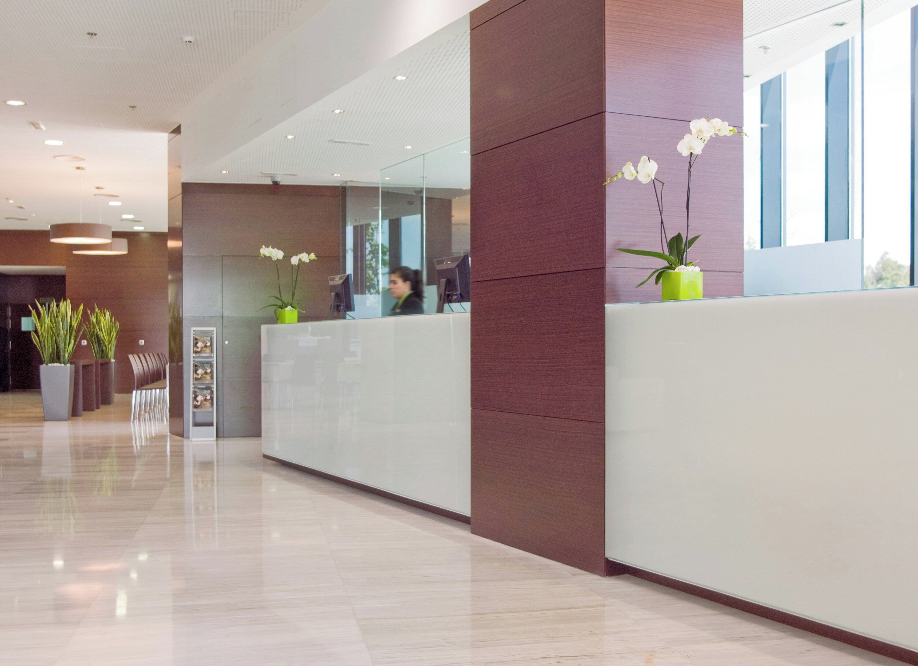 A modern reception area with a glass partition, a reception desk, and potted plants.
