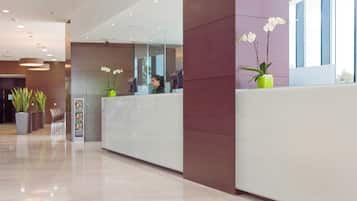 A modern reception area with a glass partition, a reception desk, and potted plants.